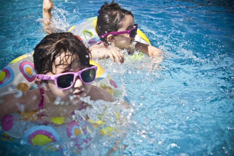 Two toddlers swimming a pool wearing sunglasses.
